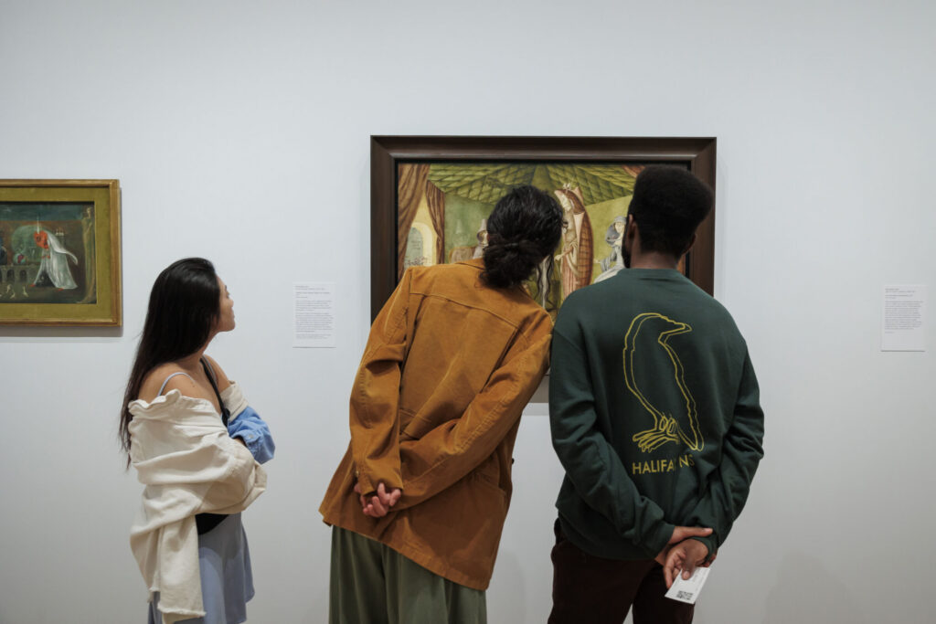 Three visitors viewing artwork inside a museum gallery.