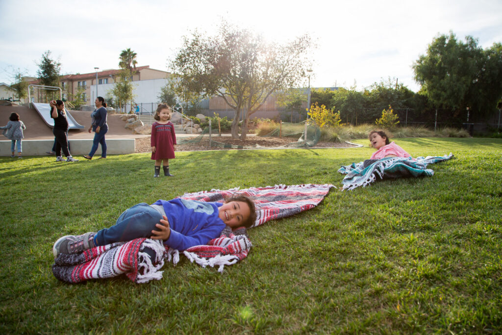 Children playing and relaxing on a grassy lawn in a neighborhood park.