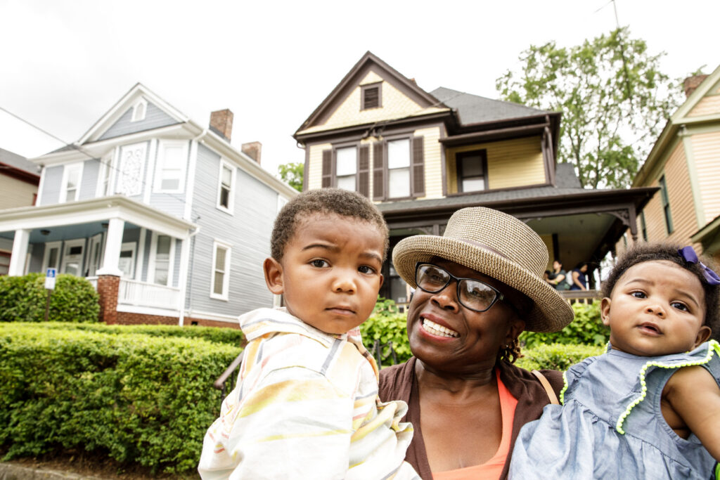 Mother and children outside a row of neighborhood homes and green space.