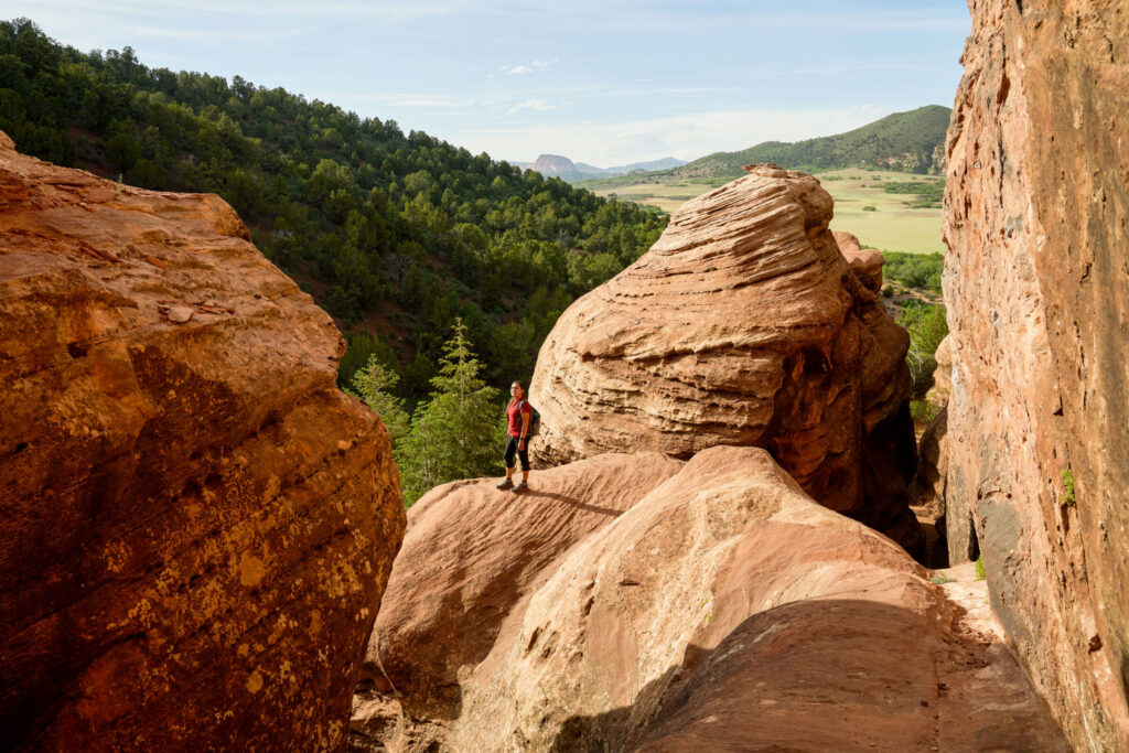 Hiker standing among red rock formations overlooking protected open landscape.